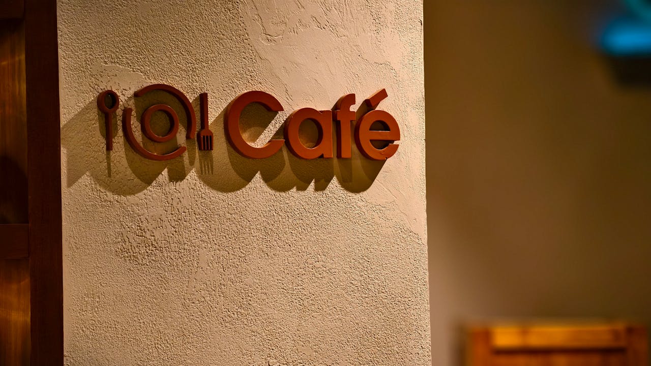 hero-img-01 Close-up of a stylish café sign with warm lighting casting shadows on a textured wall.